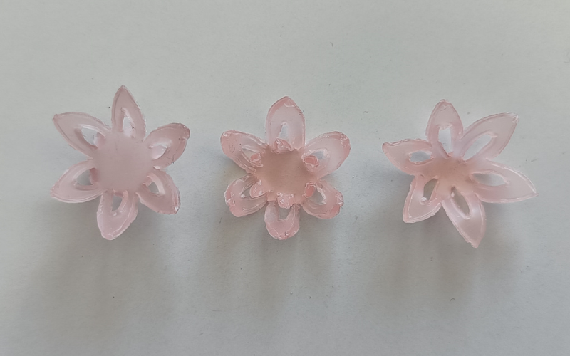 3 pink sheet wax flowers side by side. Left flower with small cutout on the petals and, middle small cutouts on the petals that are bend forward, right complete cutouts on the petals