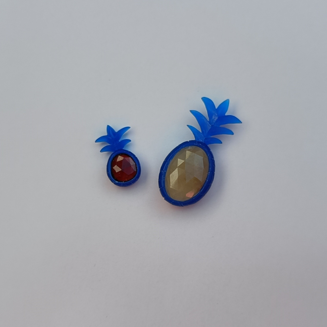 2 ananas carvings, a small one with a red center stone and a bigger one with an oval yellow stone