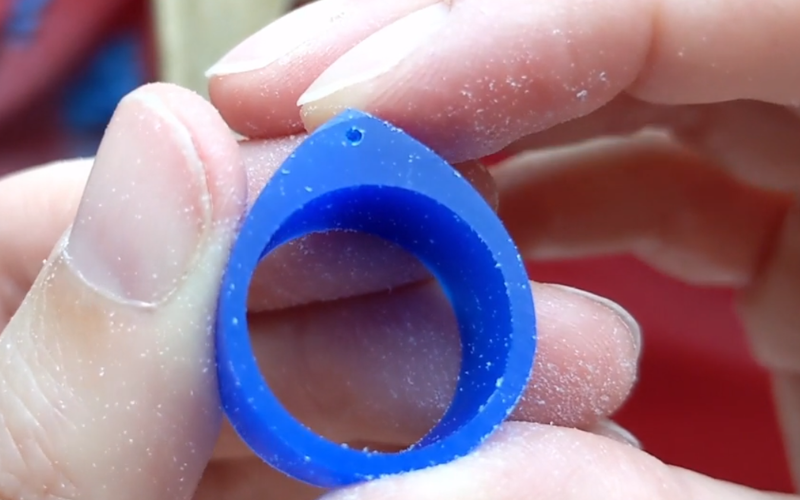 close up of hands holding a blue wax ring, side of the ring is almost perfectly flat except for one small part on the top that's been filed more because I was not keeping the file flat