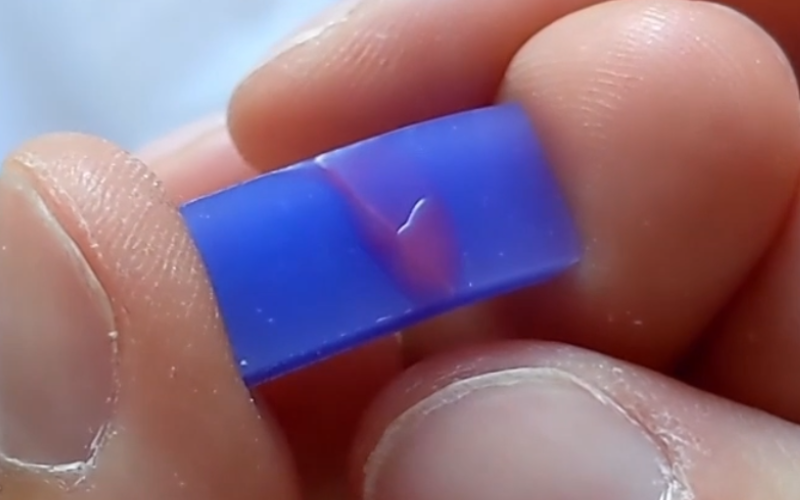 Close up of hand holding a piece of blue wax that has a break running over the surface. The break is covered with red wax. 