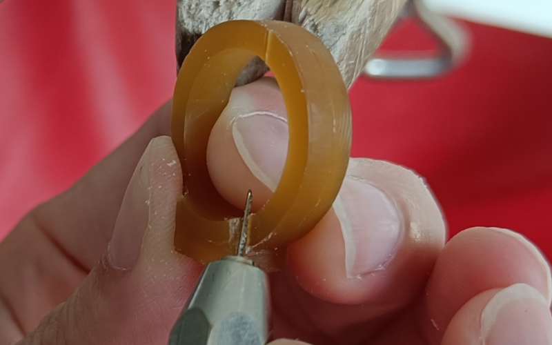 Close up of hands piercing a piece of gold wax with the smallest bit of broken saw blade in a pin vice