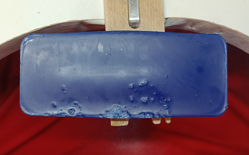 Close up of block of blue hard wax on top of a bench peg. Some airbubbles are visible on the edges from melting it in the oven 