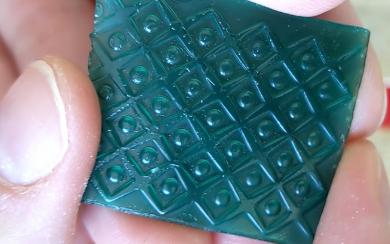 Close up of hands holding green wax sheet with a texture from rolling it in an embossing folder with a rolling pin 