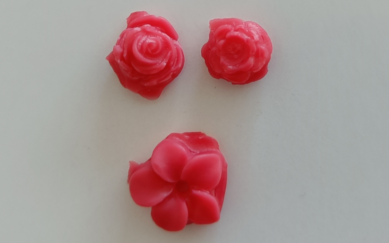 Close up of 3 flower shapes from red wax that have been made by pouring liquid wax into a mold 