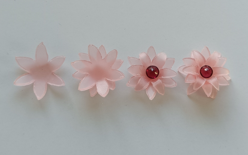 4 flowers from pink sheet wax. Left single layer 6 petal, next double layer 12 petal, next double layer bottom folds up top folds down with red stone in the center, triple layer with red stone in the center