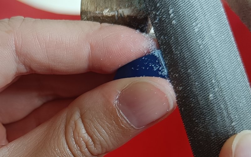 Close up of hands filing a piece of blue wax. Thumb of holding hand is right next to the file, making sure it stays on track