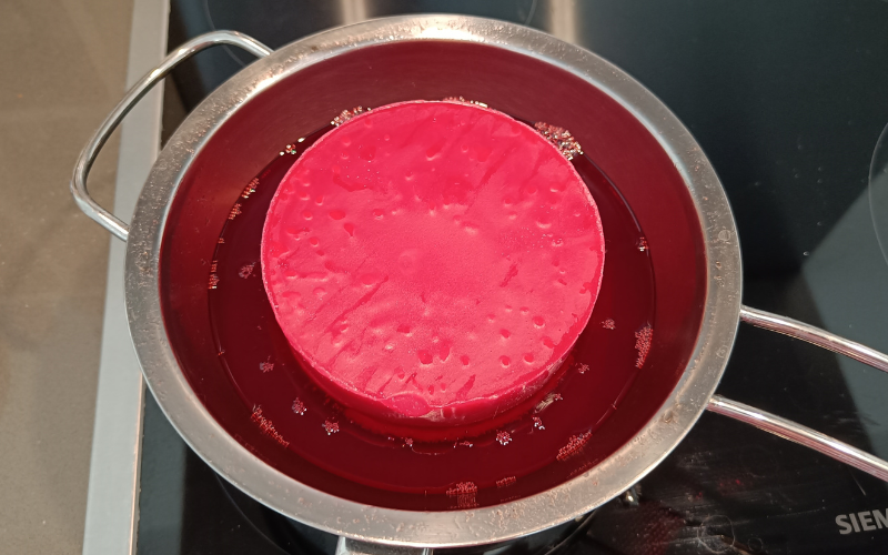 Close up of a pan with red wax inside. Middle is solid but around the edges you can see the melted wax.