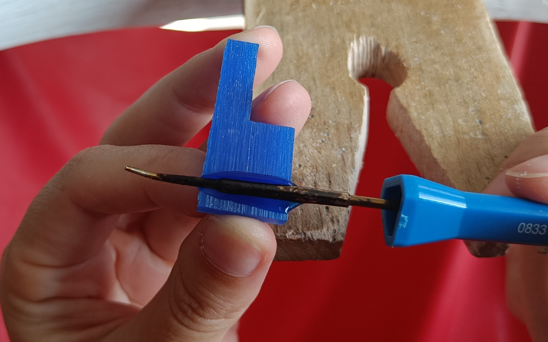 Close up of hands holding a piece of blue wax with a wax heating pen going over the piece horizontally and melting a groove in it