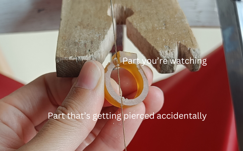 Close up of hands holding a piece of gold ring wax. Piercing up top next to a setting part and accidentally also piercing at the bottom