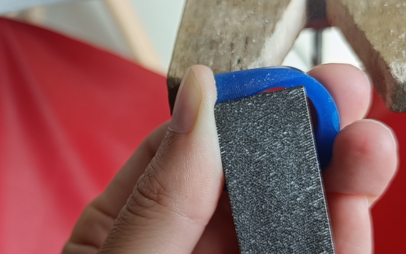 Close up of hands filing a piece of blue wax. The file is going a little bit into the meaty part of the thumb