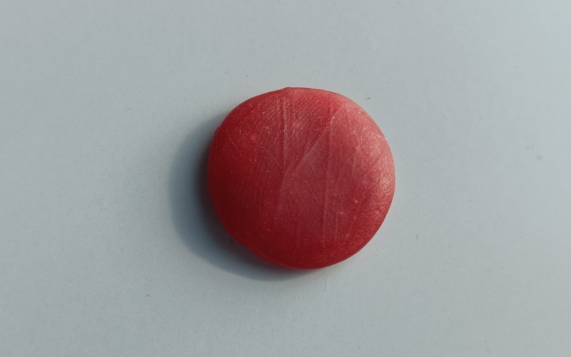 Close up of a circular piece of red wax with a palm print on top  