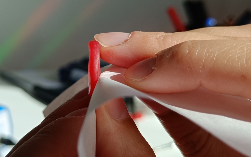 Close up of hands peeling a bit of paper away from a red wax piece 