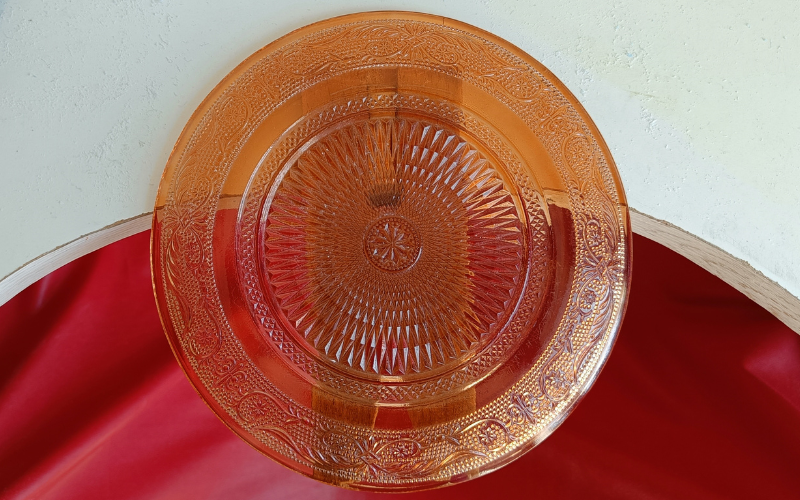 Orange colored glass plate with decorative flower patterns on the outside