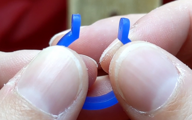 Close up of hands holding blue wax ring, a section is removed and 2 posts stick out at the top