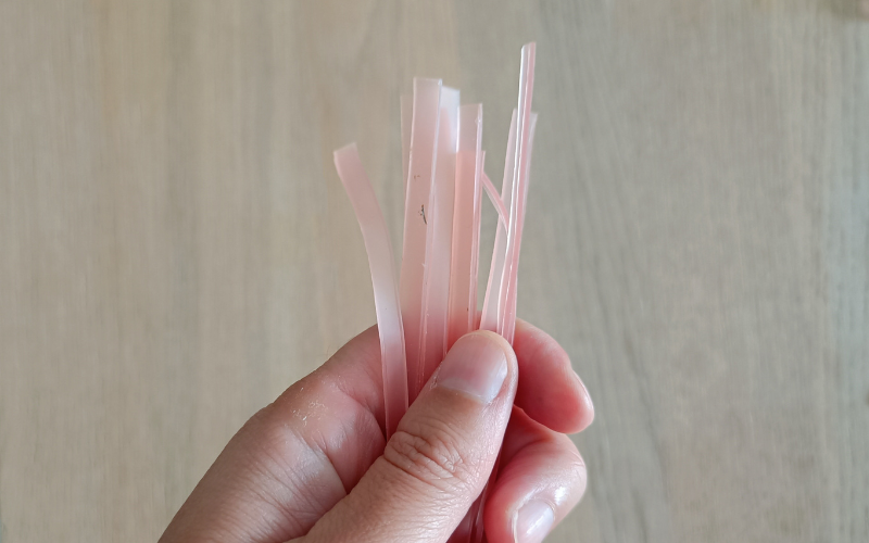 Close up of hand holding 10 thin strips of pink sheet wax