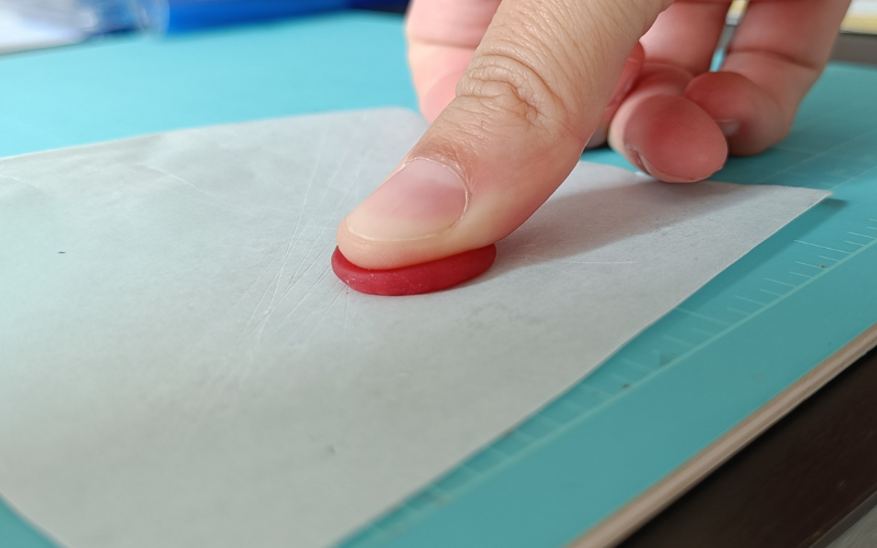 Close up of thumb pushing on top of a small bit of red wax 