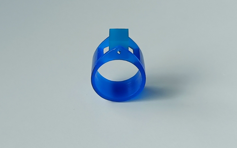 Wide blue wax ring that ends in a point on top. The center is removed and a rectangle from turquoise wax is suspended between the points of the ring 