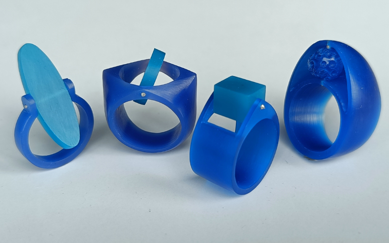 4 rings from blue wax with a turquoise wax center piece. From left to right thin band with oval center, diamond shaped signet ring with round center, wide triangular ring with rectangular center, Big ring with oval shape on top and organic shaped center