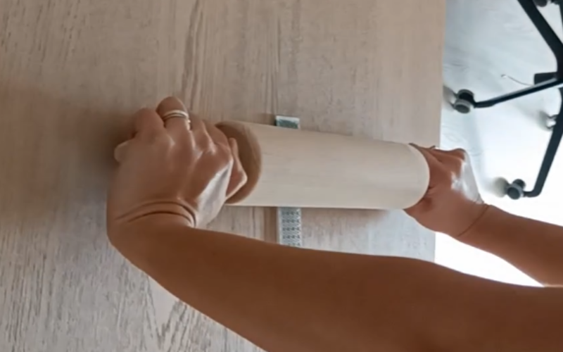 Close up of table with an embossing folder with sheet wax inside, arms are visible rolling a rolling pin over the embossing folder