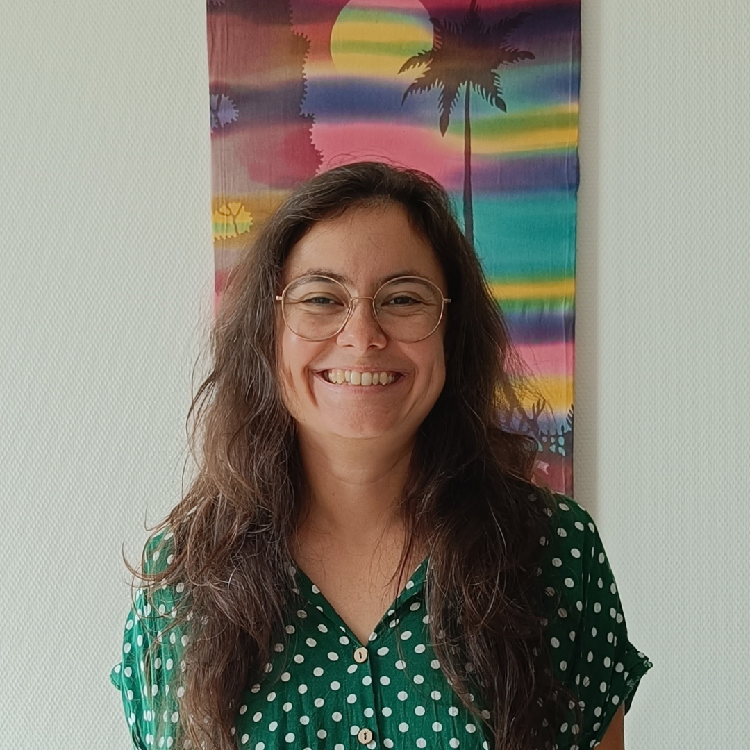 Photo of Sandy wearing a red metalsmith society shirt in front of a batik wall hanging