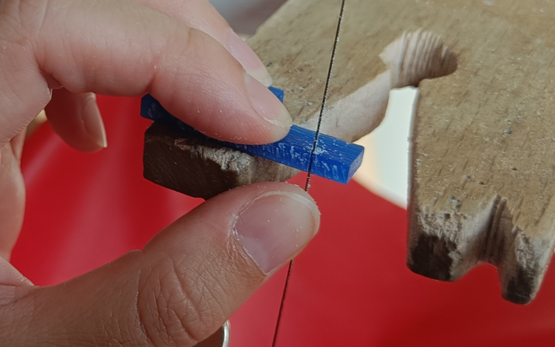 Close up of hands piercing a piece of blue wax. Thumb of holding hand is on the saw blade underneath the wax to steer it in the right way