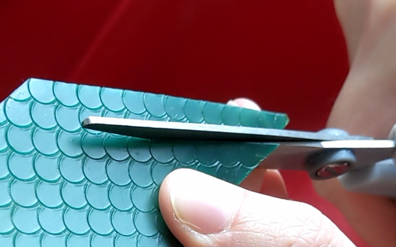 Close up of hands cutting through green sheet wax with scissors 