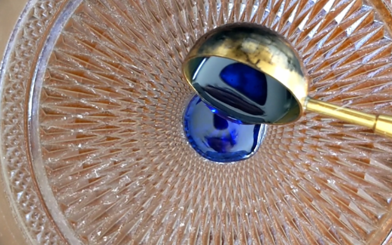 Close up of glass plate, a spoon with melted hard blue wax is being poured over the plate