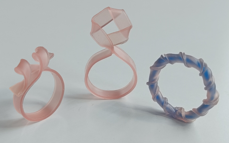 3 rings from strips of pink sheet wax. One with a twist, one with a folded part that stand up one completely twisted with a blue wire in the center 