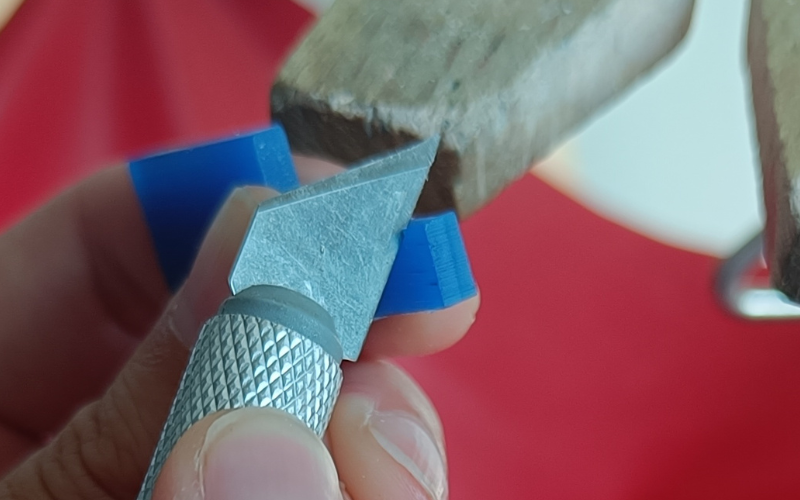 Close up of blue piece of wax with a stanley knife slicing the side with the opposite side of the blade