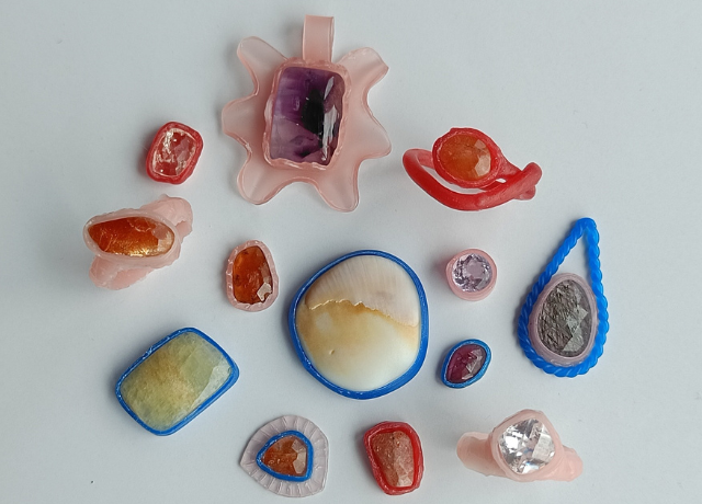 A collection of 13 different settings pieces on a white background. The pieces are made from pink sheet wax, blue wire wax, and red wax.