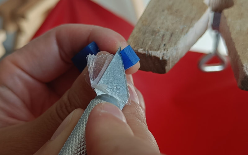 Close up of a blue piece of wax with a stanley knife slicing in it. The stanley knife is taped off partially