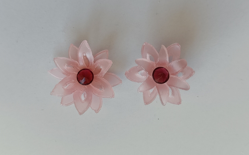 2 pink sheet wax flowers with double layers and cut outs on one of the layers. A red gemstone is placed upside down in the center. 