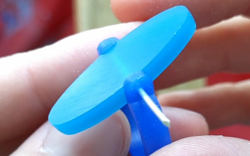 Close up of hands holding a thing blue wax ring with a piece of turquoise wax suspended at a 45 degreeish angle in the middle