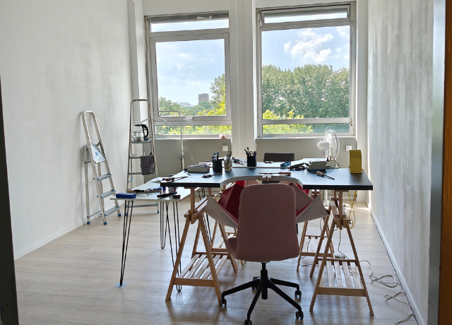 Studio space with big windows in the back, home made jewellery bench set up with a few tools and ladders in the background
