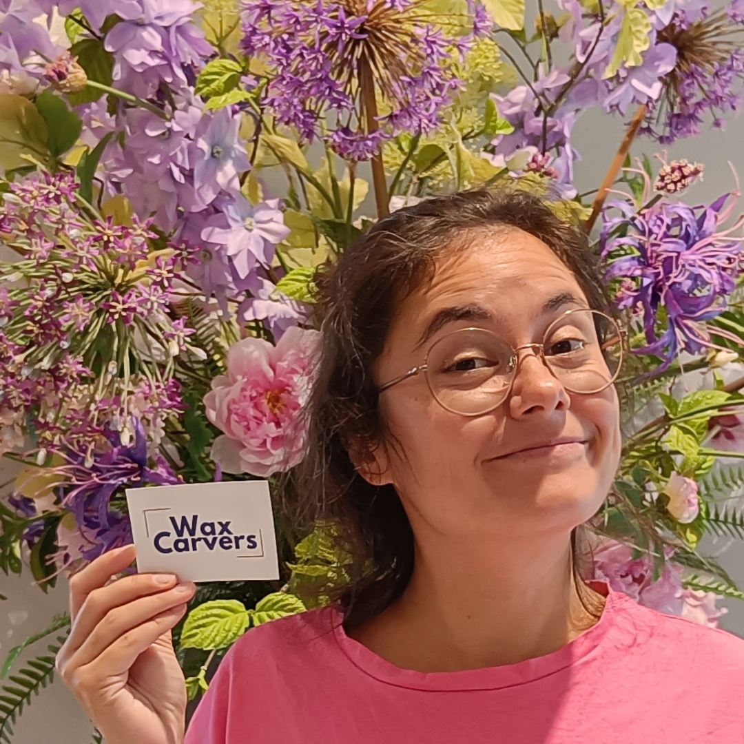 Close up of Sandy holding a Wax carvers sticker in front of a purple bouquete of flowers